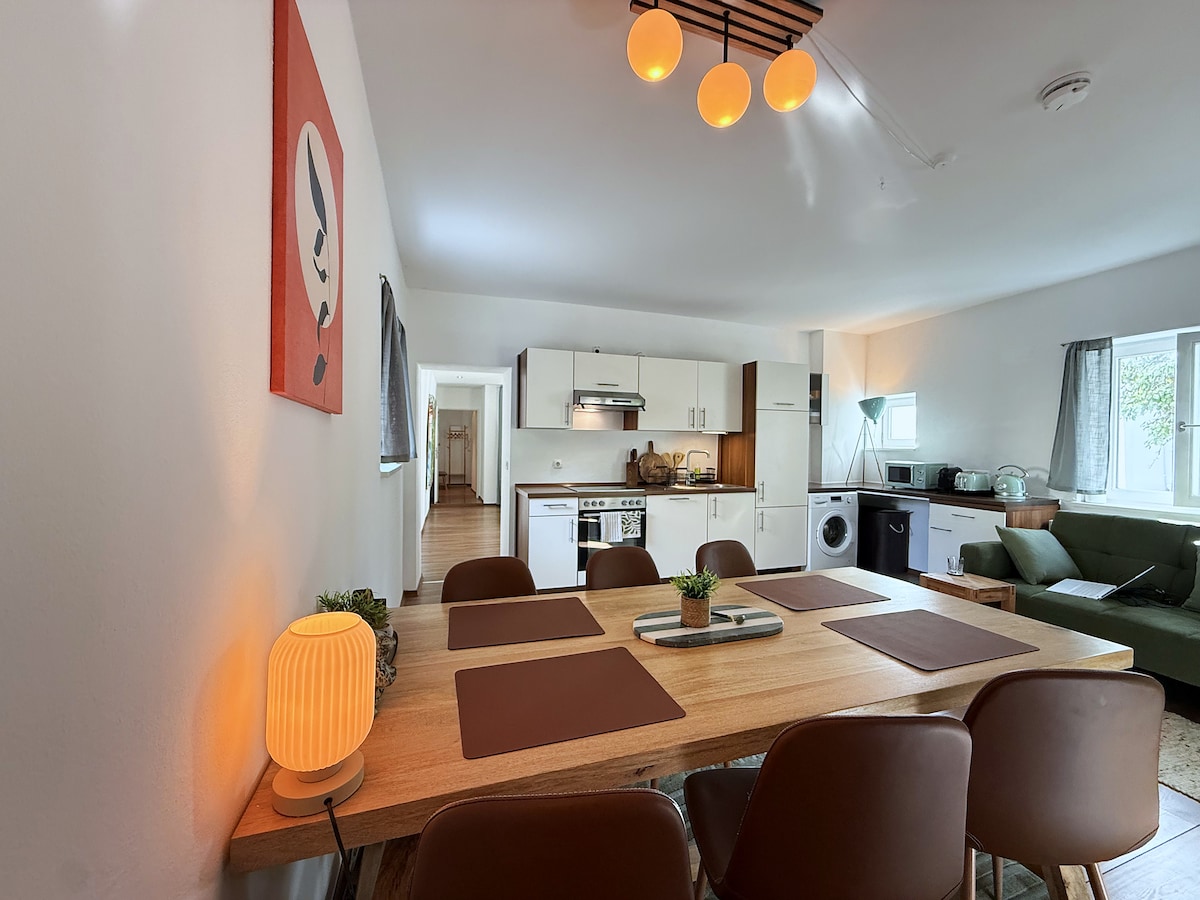 The 2 m wooden table with placemats, the kitchen and the hallway behind it