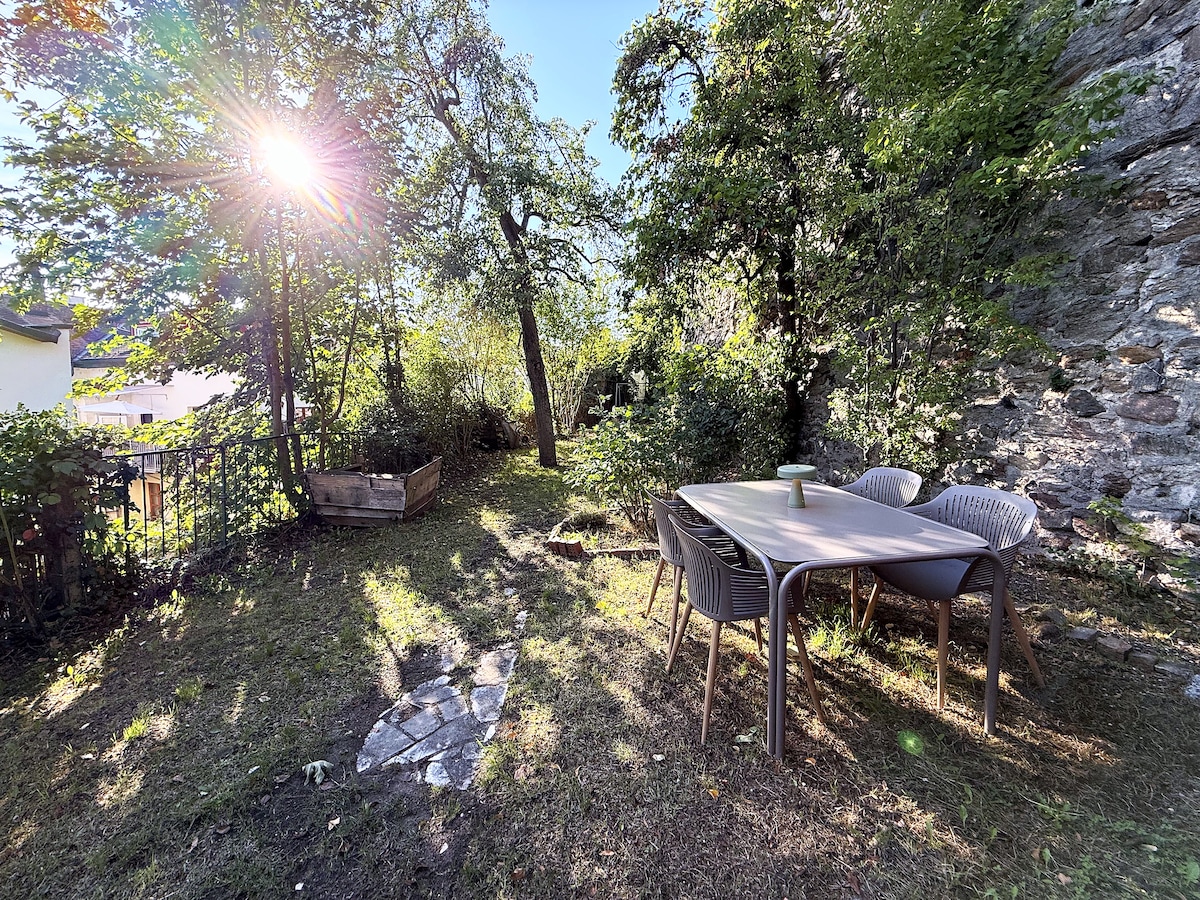 Garden table and chairs on the lawn under the trees, the old wall behind