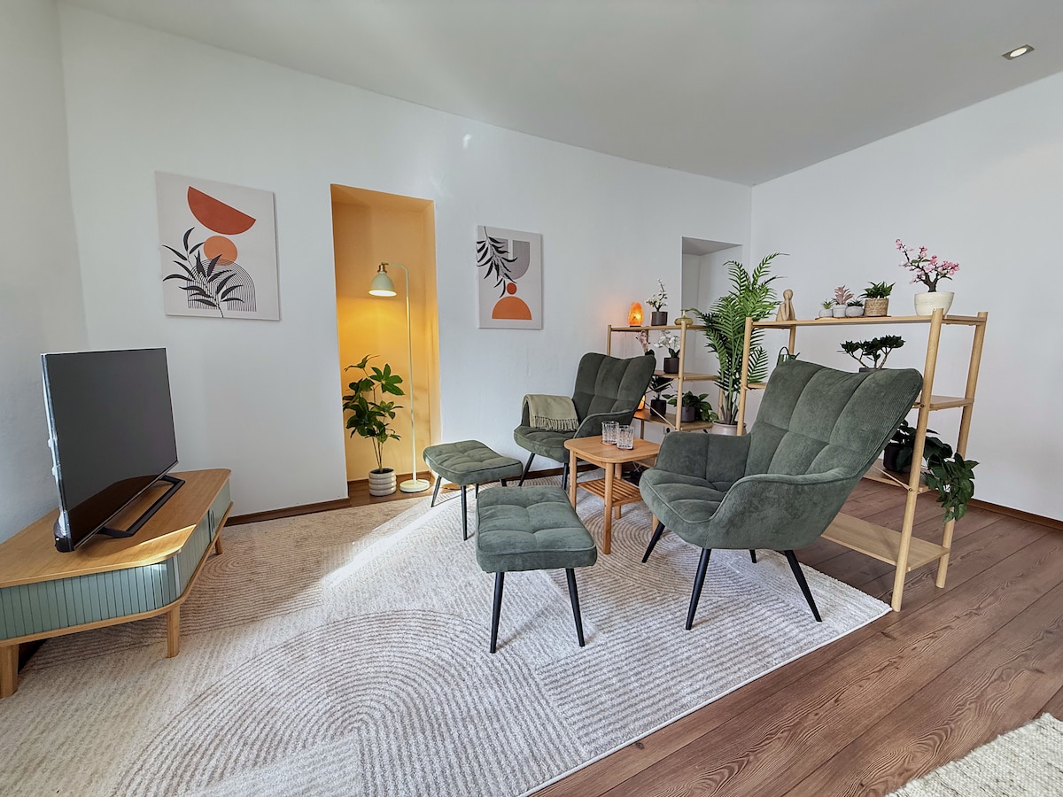 Living room with two armchairs with footstools, the plant shelf and the TV on the sideboard